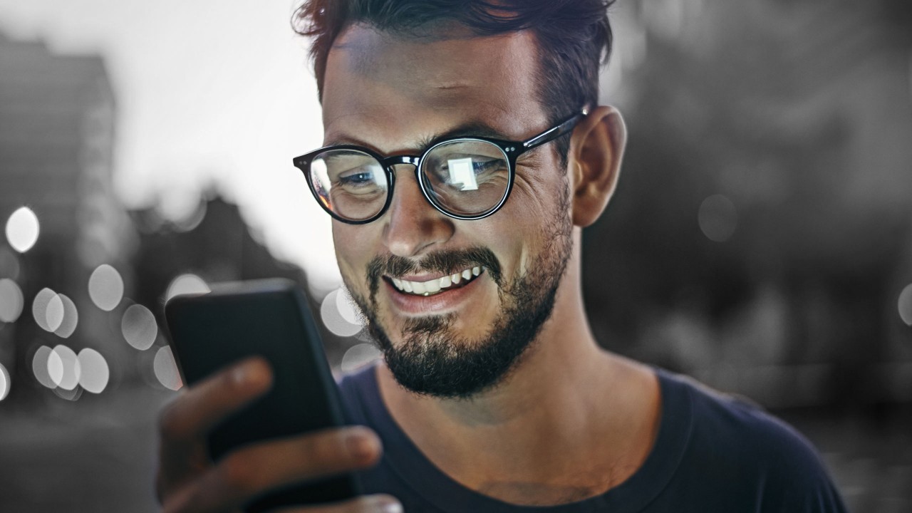 A young man smiling and reading email in his phone; image used for HSBC Australia Using a personal loan to fund your MBA.