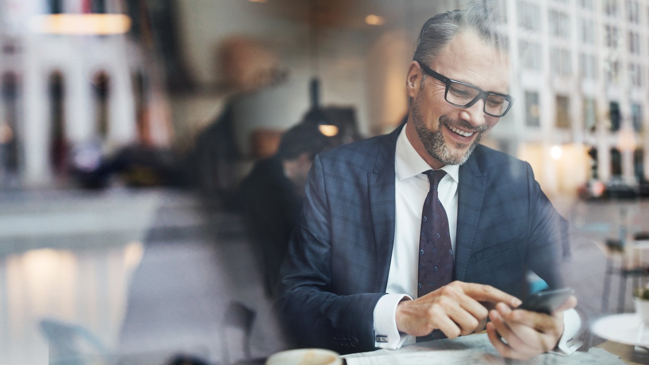 A mature businessman sitting inside at cafe and using phone; image used for HSBC Guide to international transfers.