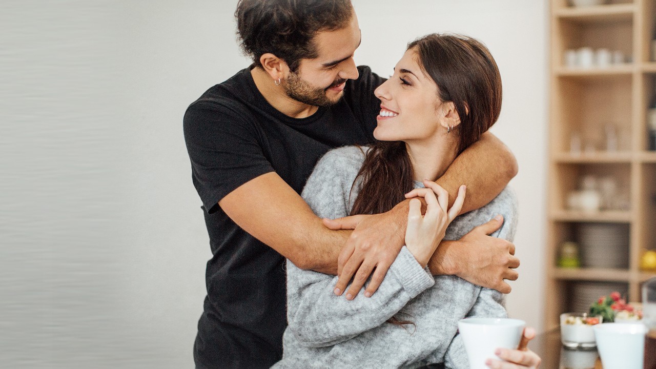 A romantic couple embracing in the kitchen; image used for HSBC How to save up for a house deposit.