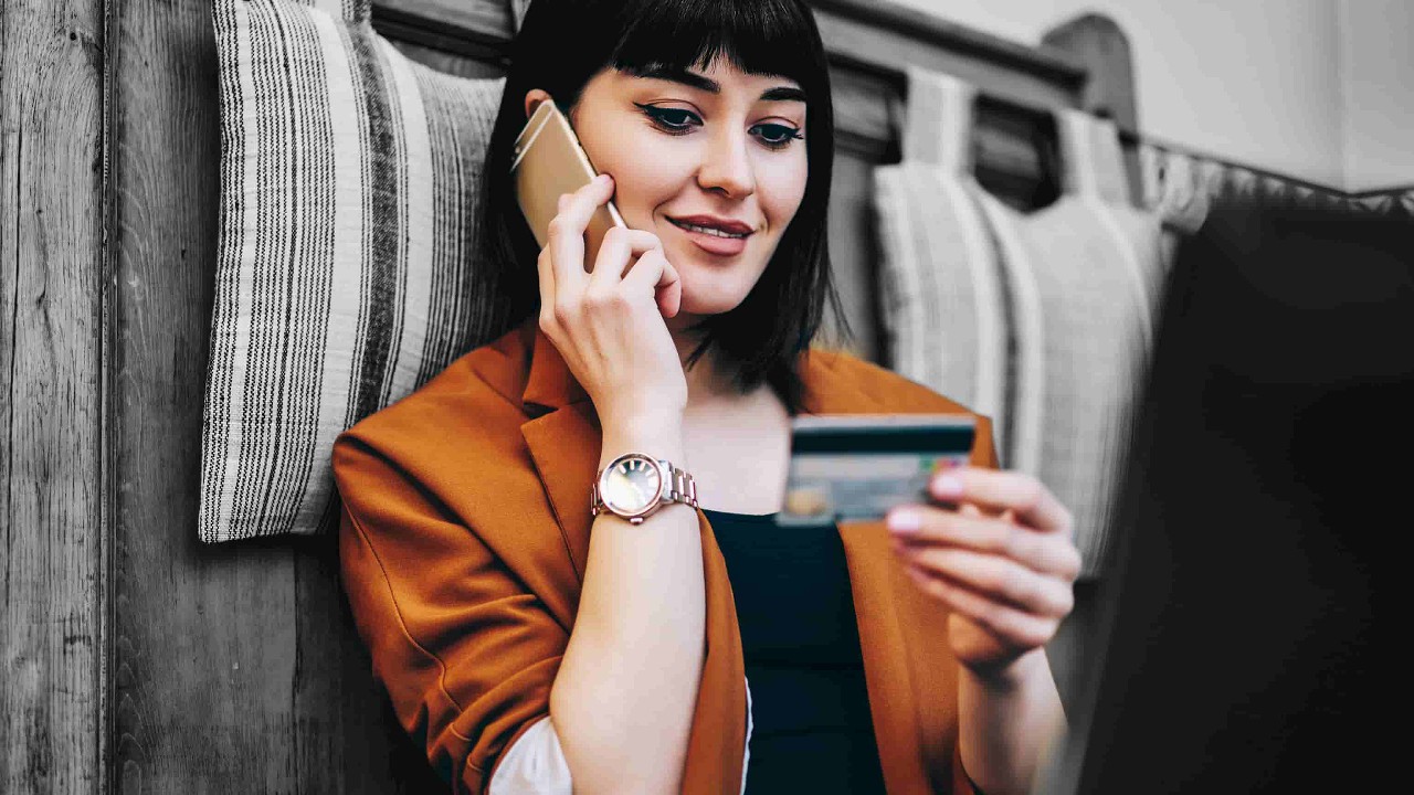 A lady is looking at her credit card while she's on the phone; image used for understanding credit card interest page.