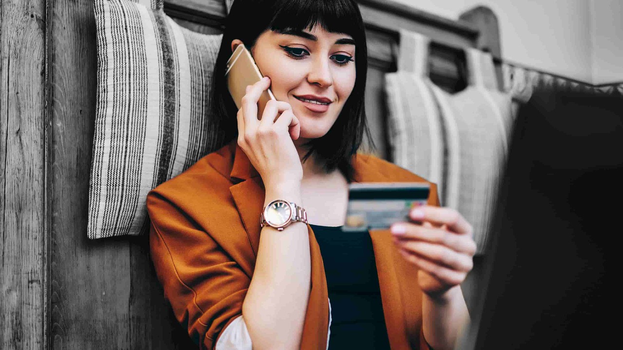 A lady is looking at her credit card while she's on the phone; image used for understanding credit card interest page.