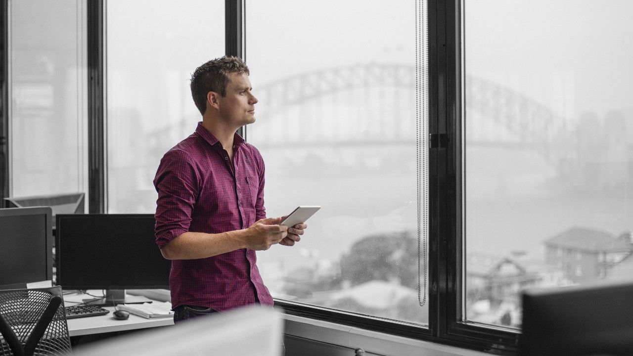 A man holding tablet and staring out of window; image used for HSBC Foreign Currency Flexi Saver Account page.