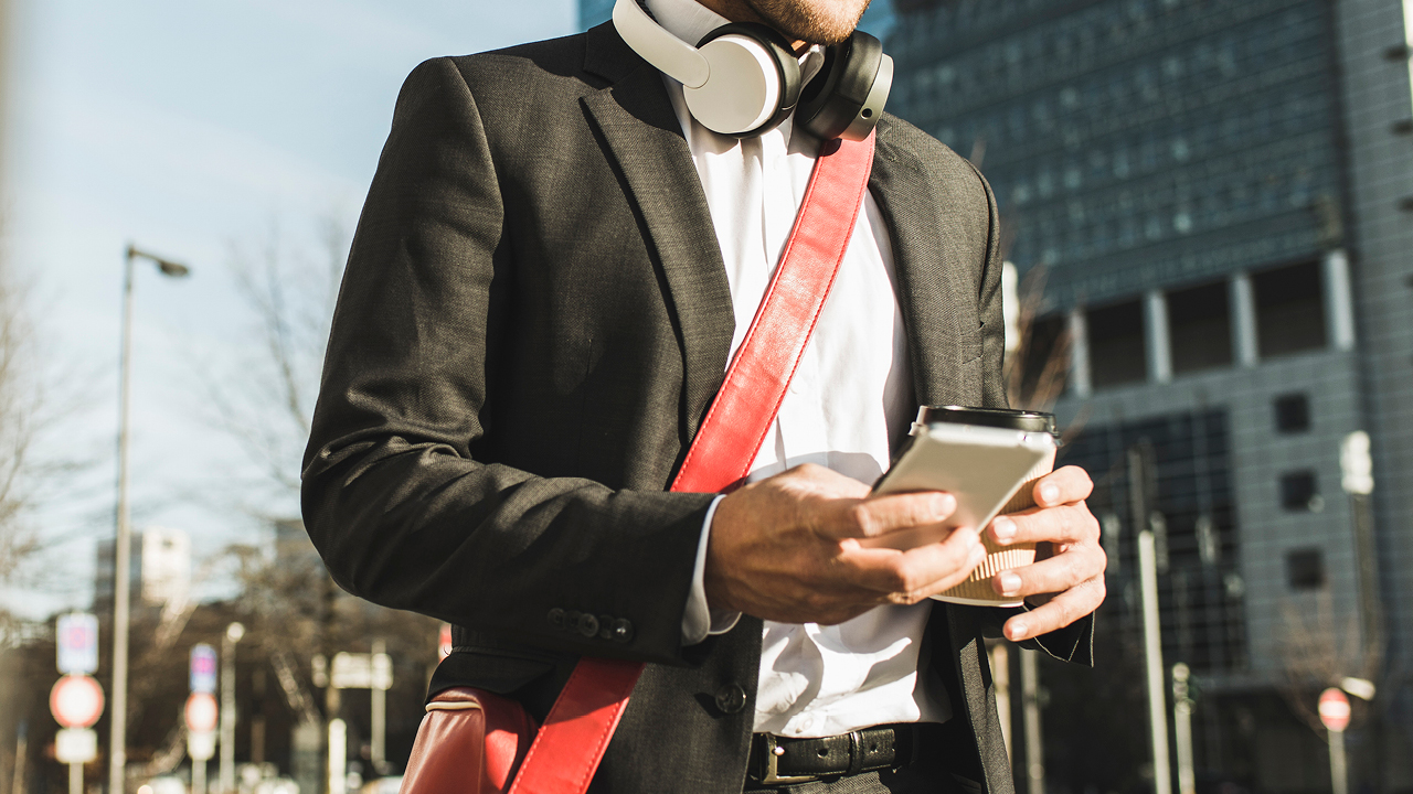 Man using phone while walking with headphones on his neck; image used for HSBC Australia Phone Banking.