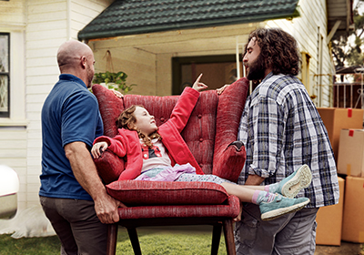 Two men moving a couch with a little girl sitting on it into a house; image used for HSBC Australia's Home Loans product.