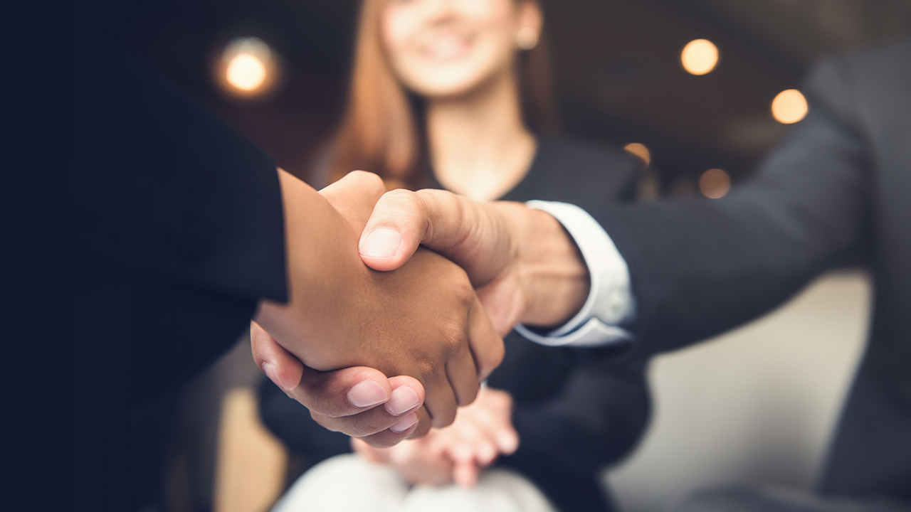 Two people are shaking hands while a girl is sitting in the background; image used for HSBC Markets Desk.