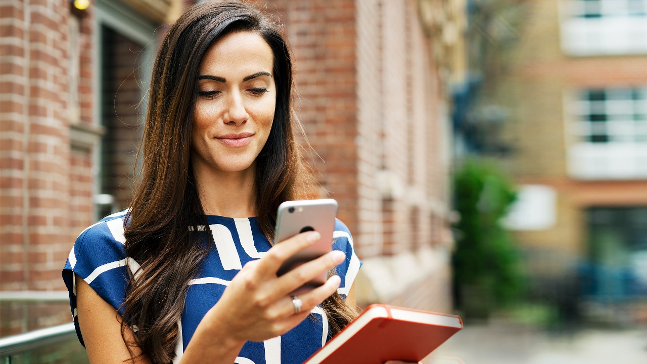 A woman using smart phone on the street; image used for HSBC Essential foreign exchange travel tips.