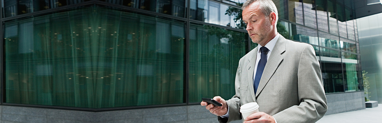 Businessman checking phone with a cup of coffee; image used for HSBC Australia trading platform.