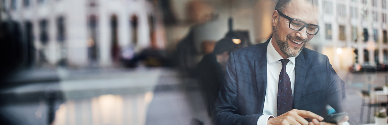 A mature businessman sitting inside at cafe and using phone; image used for HSBC Guide to international transfers.