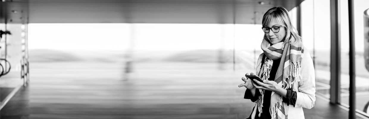 Businesswoman with smart phone standing at the airport; image used for HSBC Australia FAQs.