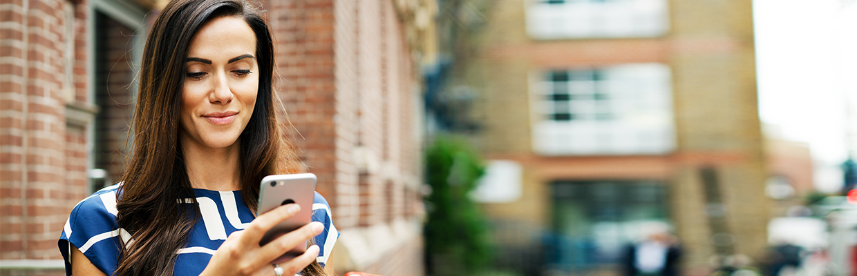 A woman using smart phone on the street; image used for HSBC Essential foreign exchange travel tips.