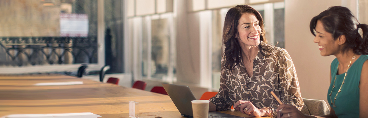 Two women are discussing happily in the office in front of the laptop; image used for HSBC's Employee Banking Solutions Program