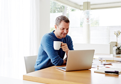 A man using computer with a coffee in his hand; image used for HSBC Australia coronavirus (COVID-19) guidance and support article page.